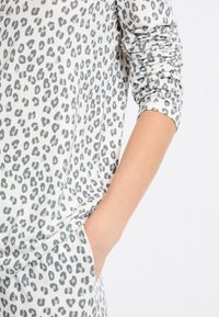 Dlouhý rukáv top v světle šedé látce s tmavě šedým leopardím potiskem, s volnějším střihem a boční kapsou. Texturovaný, měkký materiál.