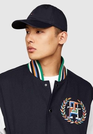 Marineblauer College-Jacket mit geripptem, mehrfarbigem Kragen, der ein gesticktes Logo mit verflochtenen Initialen und Lorbeerakzenten zeigt.