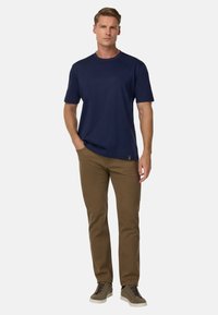 Tyrkysové tričko s krátkým rukávem, doplněné hnědými kalhotami. Má kulatý výstřih a hladkou, lehkou tkaninu.