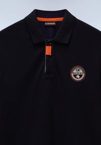 Svart polo t-shirt i strukturerad tyg, med en kontrasterande orange rand på kragen, tre knappar och en rund logotyp på bröstet.