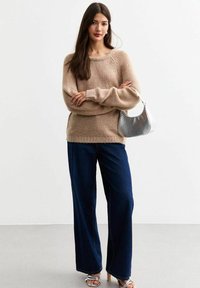 Beige stickad tröja med vid halsringning och luftiga ärmar, kombinerad med mörkblå vida jeans och en silverhandväska. Släta texturer överlag.