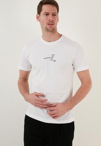 White cotton T-shirt with short sleeves, featuring black text across the front. Smooth texture, round neckline, and relaxed fit.