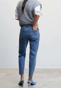 Jasnoniebieskie, wysokie jeansy o prostym kroju, z tylnymi kieszeniami, w połączeniu z szarym swetrem bez rękawów i niebieskimi sandałami na obcasie.