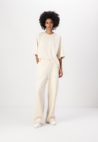 Beige oversized t-skjorte med korte ermer, kombinert med matchende vide joggebukser med elastisk midje og subtil logo-detalj.