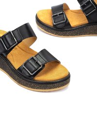 Sandalias negras con dos correas ajustables, hebillas plateadas y una plantilla de corcho. La suela tiene una textura con un acabado negro moteado.