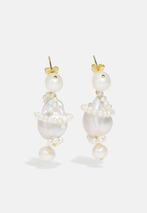 Σκουλαρίκια με σταγόνες από μαργαρίτες που διαθέτουν ακανόνιστα σχήματα μαργαριταριών, μικρές προσαρτήσεις από μαργαριτάρια και χρυσά υλικά με λεπτομέρεια βρόχου στην κορυφή.