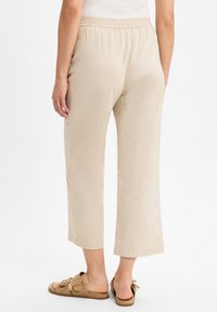 Lichtbeige, loszittende broek met een elastische tailleband, cropped lengte en een gladde textuur, gecombineerd met bruine sandalen met open tenen.