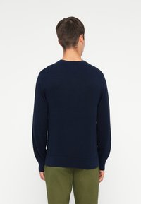 Suéter azul-marinho de malha com mangas longas, gola redonda, punhos e bainha canelados. Feito de um tecido macio, com um corte descontraído.