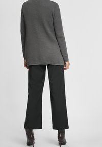 Gray textured long-sleeve top with a loose fit, paired with black wide-leg trousers. The outfit is completed with dark heeled boots.