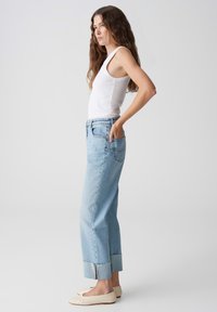 Jeans azzurri a vita alta con gamba dritta e orli risvoltati, indossati con un top bianco senza maniche e scarpe basse beige.