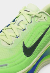 Gros plan sur une chaussure de sport vert vif avec un logo Nike noir, des lacets vert clair, et des accents bleus et verts sur la semelle.