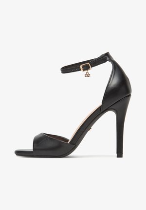 Schwarze Sandaletten mit hohen Absätzen und offenem Zehenbereich, elegantes Design. Verfügt über einen Knöchelriemen mit goldener Schnalle und hängendem "DZ"-Anhänger. Glatte Lederstruktur.