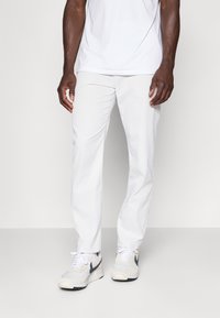 Vita byxor med slim fit design, slät textur, bälteshällor och sidofickor, som är kombinerade med en enkel vit skjorta och sneakers.