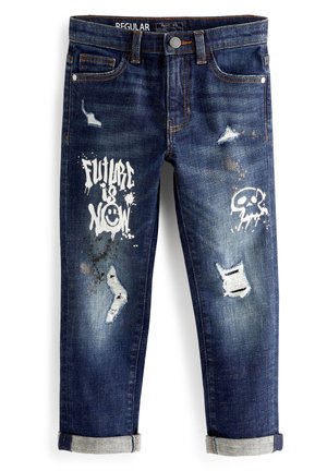 Vaqueros desgastados azul oscuro con puños remangados, texto en grafiti blanco "El futuro es ahora", una cara sonriente y un gráfico de calavera en las piernas delanteras.