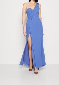 Jednoduché modré maxi šaty s jedním ramenem, s těsným korzetem, drapovanou texturou a rozparkem po stehna. Hladká látka, elegantní silueta a minimální akcenty.