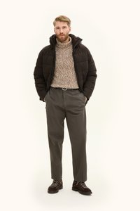 Zwarte pufferjack met hoge kraag, gebreide beige trui, grijze broek en bruine veterschoenen met donkere accenten.