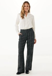 Camicia bianca con bottoni abbinata a pantaloni larghi a quadri bianchi e neri. I pantaloni presentano un tessuto testurizzato e tasche laterali. Scarpe nere.