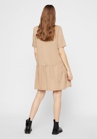 Abito beige a maniche corte con orlo arricciato, realizzato in tessuto morbido, caratterizzato da una vestibilità comoda e indossato con stivali neri alla caviglia.