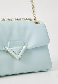 Sac à main en simili cuir bleu clair avec un accent en métal géométrique à l'avant, doté d'une chaîne de portée et d'une texture lisse.