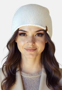 Cremefarvet strikket beanie med ribbet tekstur, foldet kant og en lille brun accent på siden.