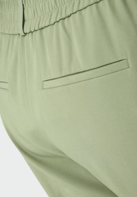 Heledad rohelised püksid pehmest kangast, millel on kogutud vöökoht ja kaks kitsast, lamedat Taskut taga. Sile tekstuur.