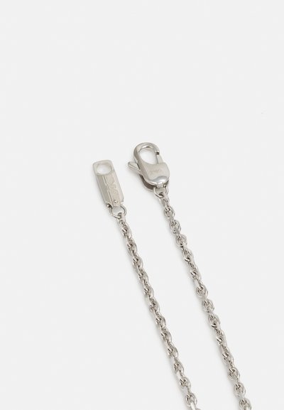 Stříbrný metalový řetěz s karabinkovým zapínáním a malou dekorativní visačkou. Řetěz má uniformní články a lesklý, leštěný povrch.