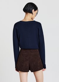 Marineblauer Strickpullover mit lockerem Schnitt und weitem Ausschnitt, kombiniert mit braunen Cord-Hochbundshorts mit Gesäßtaschen und strukturierter Oberfläche.