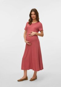Un abito premaman lungo fino al ginocchio in morbido tessuto rosa, con scollatura rotonda e maniche corte, dalla vestibilità ampia che scivola dalla vita.