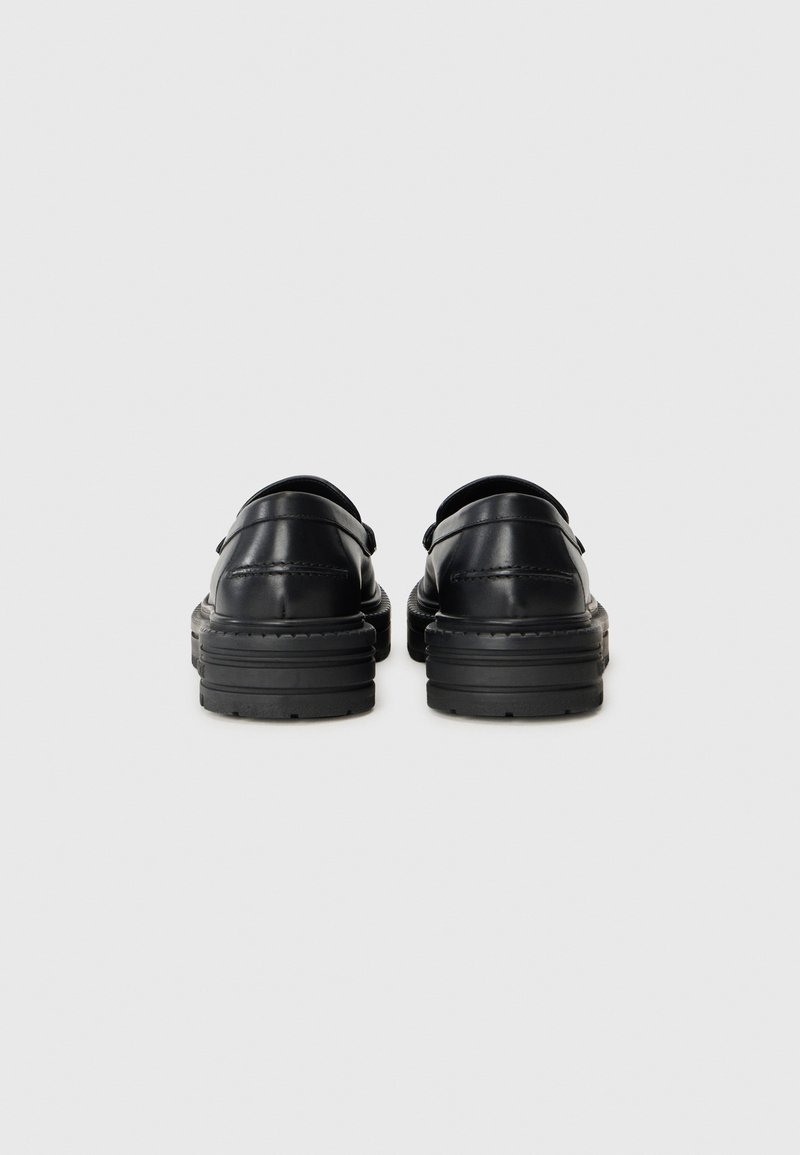 Chaussures en cuir noir avec une finition lisse, forme arrondie et semelles en caoutchouc épaisses. Présentent des coutures minimales et aucun matériel visible.