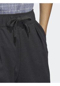 Mustat joustovyötäröiset housut, joissa on teksturoitu kiristysnyöri ja sivutaskut; kangas näyttää sileältä ja hieman kiiltävältä, löysillä laskoksilla.