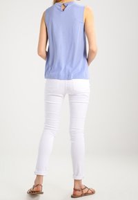 Vaaleansininen hihaton toppi, jossa on takana avainreikädetaili, yhdistetty istuviin valkoisiin farkkuihin ja litteisiin sandaaleihin. Sileä pinta ja rento muotoilu.