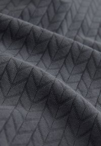 Stof met een gestructureerd visgraatpatroon in donkergrijs. Het materiaal lijkt zacht met een subtiel, verhoogd ontwerp.