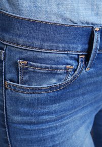 Jeans de mezclilla azul con una textura desgastada, que cuentan con un bolsillo trasero con costuras visibles y un diseño ajustado.