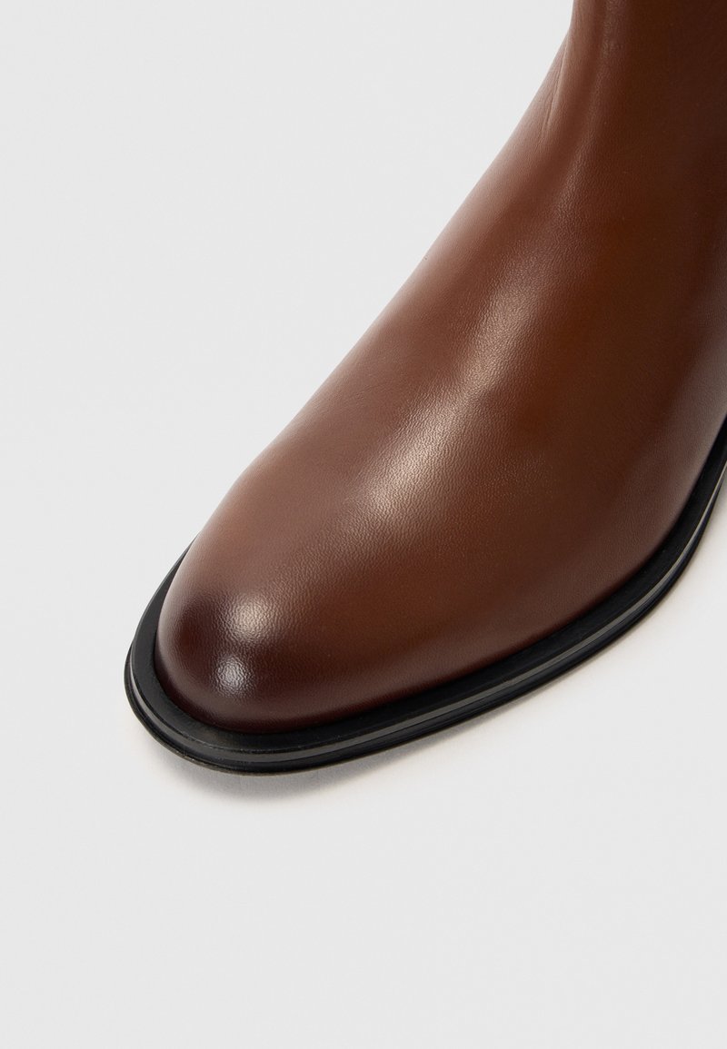 Stivale alla caviglia in pelle marrone con un design elegante, punta a mandorla e bordatura nera della suola. La superficie ha una finitura liscia con una leggera lucentezza.
