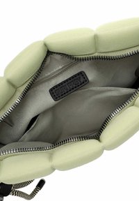 Interno della borsa imbottita verde con cerniera argentata, dotato di un'etichetta "SURI FREY" e una tasca con cerniera, realizzato in tessuto morbido.