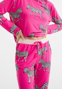 Conjunto de loungewear rosa que incluye una blusa de manga larga y pantalones. Ambos están adornados con patrones de cebra en blanco y negro. Tejido suave con cinturilla elástica.