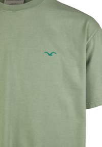 Hellegrünes T-Shirt aus Bio-Baumwolle mit Rundhalsausschnitt und kleinem, türkisfarbenem, gesticktem Logo auf der Brust. Weicher Stoff, kurze Ärmel.