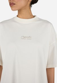 White cotton t-shirt with a crew neck, featuring printed text "Pegador" and "Scent of Summer" in light beige. Loose-fitting design.