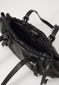 Schwarze Lederhandtasche mit gerafftem Öffnungsbereich, zwei verstellbaren Trägern und silbernen Hardware-Akzenten. Glatte Textur mit geräumigem Innenraum.