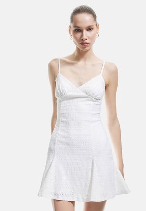 Vestido blanco con un corsé ajustado y falda acampanada. Hecho de una tela texturizada con pequeños patrones. Tirantes delgados y escote en V.