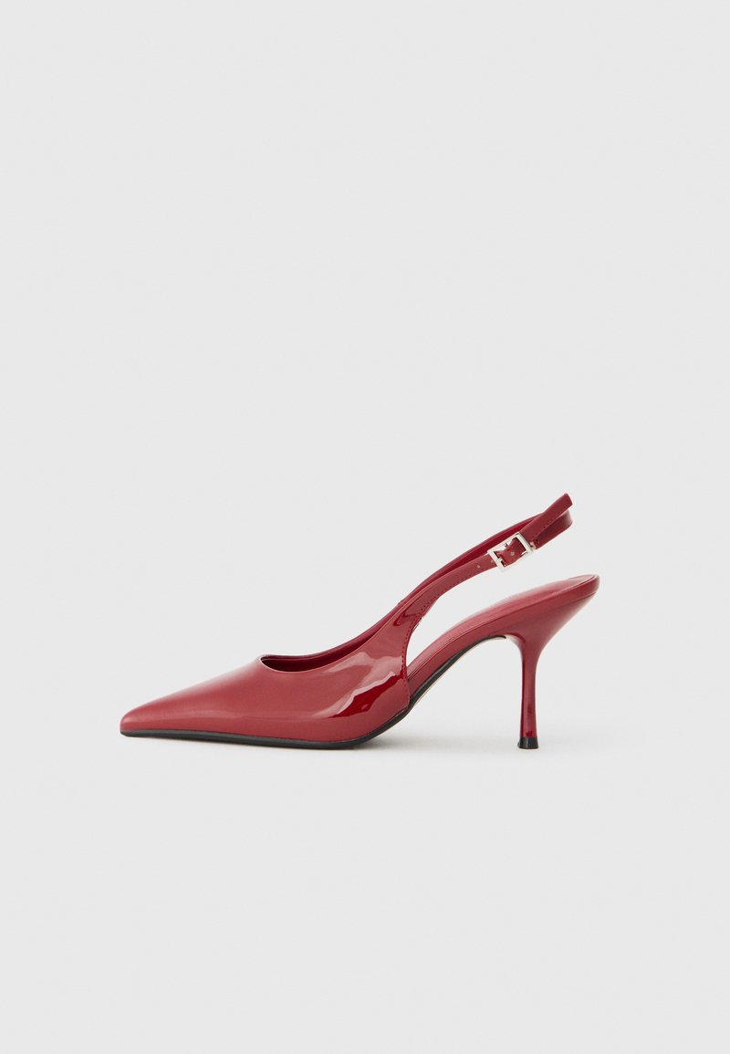 Talons aiguilles en cuir verni rouge avec un bout pointu, un talon stiletto fin et un petit détail découpé sur le côté. Texture lisse.