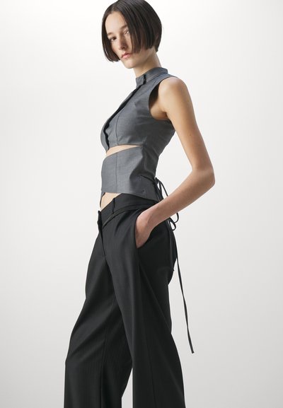 Gray sleeveless top with a high collar and cut-out detail, paired with black wide-leg trousers featuring a tie detail and side pockets.