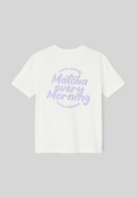 T-shirt en coton blanc avec un graphisme circulaire lavande sur lequel est écrit "plus d'énergie Matcha chaque matin, plus de pleine conscience." Manches courtes.