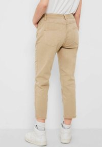 Pantalones beige hasta el tobillo de algodón, con bolsillos traseros y un corte ajustado, combinados con zapatillas altas blancas.