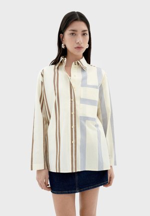 Chemise rayée jaune clair, avec des rayures verticales marron et bleu, un devant à boutons, et une poche poitrine, fabriquée en tissu tissé.