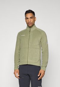 Giacca in fleece di un verde oliva chiaro, con colletto alto, zip intera e tasche laterali con dettagli cuciti; tessuto testurizzato.