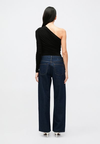 Čierny top s jedným ramenom a nariasenou textúrou, kombinovaný s vysokým pásom, širokými tmavými rifľami s vreckami na zadnej strane a jemným vyblednutím.