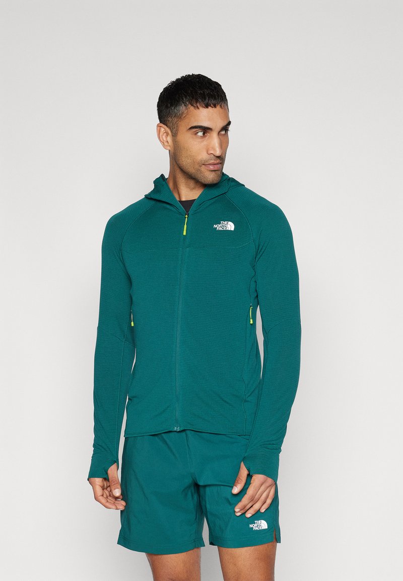 Hooded zip-up jacket in textured teal fabric with yellow zipper accents and logo. Paired with matching shorts, showcasing a sporty design.