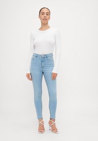 Blugi subțiri din denim albastru cu talie înaltă, cu buzunare frontale și o nuanță deschisă. Asortați cu un top alb ajustat cu mânecă lungă și sandale cu bretele.