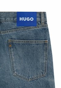 Jeans in denim con etichetta HUGO blu, una tasca posteriore con cuciture a contrasto e un taglio classico in un lavaggio blu medio.